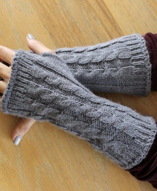 A person wearing grey knitted gloves on top of a wooden table.