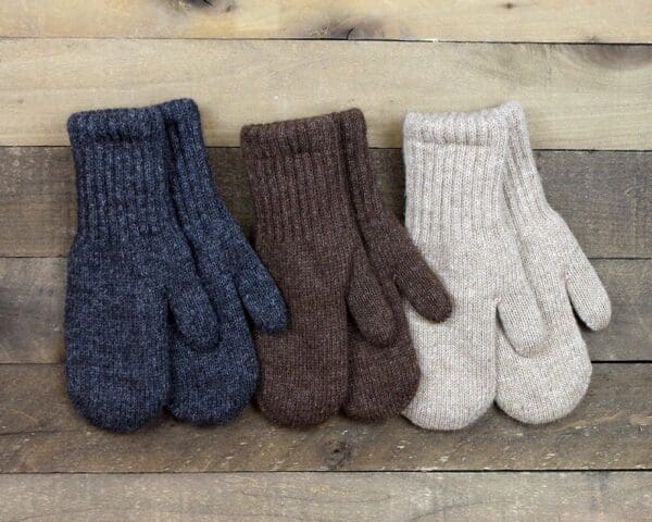 Three pairs of mittens are lined up on a wooden surface.